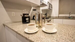 A kitchen with two white cups of coffee on a granite countertop, a black kettle, a blender, and a stainless steel coffee pot. - Modern Townhouse in the Heart of Mixcoac! (Ciudad de México)