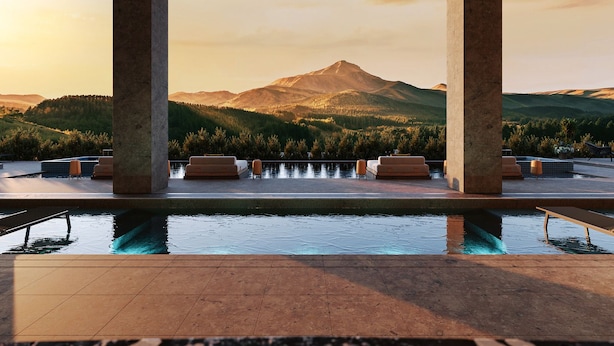 Un área de piscina con vista a la montaña, mobiliario para sentarse y cielo despejado.