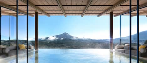 A modern infinity pool with a mountain view, wooden ceiling, and comfortable seating.