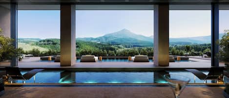 A modern indoor pool area with a view of a mountain range.