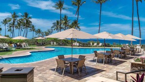 Un espace aménagé au bord de la piscine, avec des chaises longues, des parasols et une vue sur l’océan.