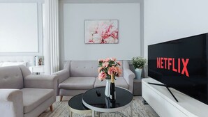 A modern living room with a sofa, a coffee table with a vase, a TV displaying 'NETFLIX,' and a wall-mounted picture. - D'. El Dorado Ho Tay Luxury Apartment  (Hanoi)