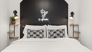 Une chambre à coucher avec une tête de lit noire, deux tables de chevet avec des lampes, un néon et des coussins à motifs.