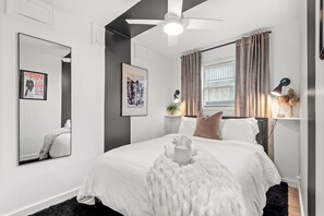 Ein modernes Schlafzimmer mit einem großen Bett, einem Deckenventilator und einem Fenster mit Vorhängen.