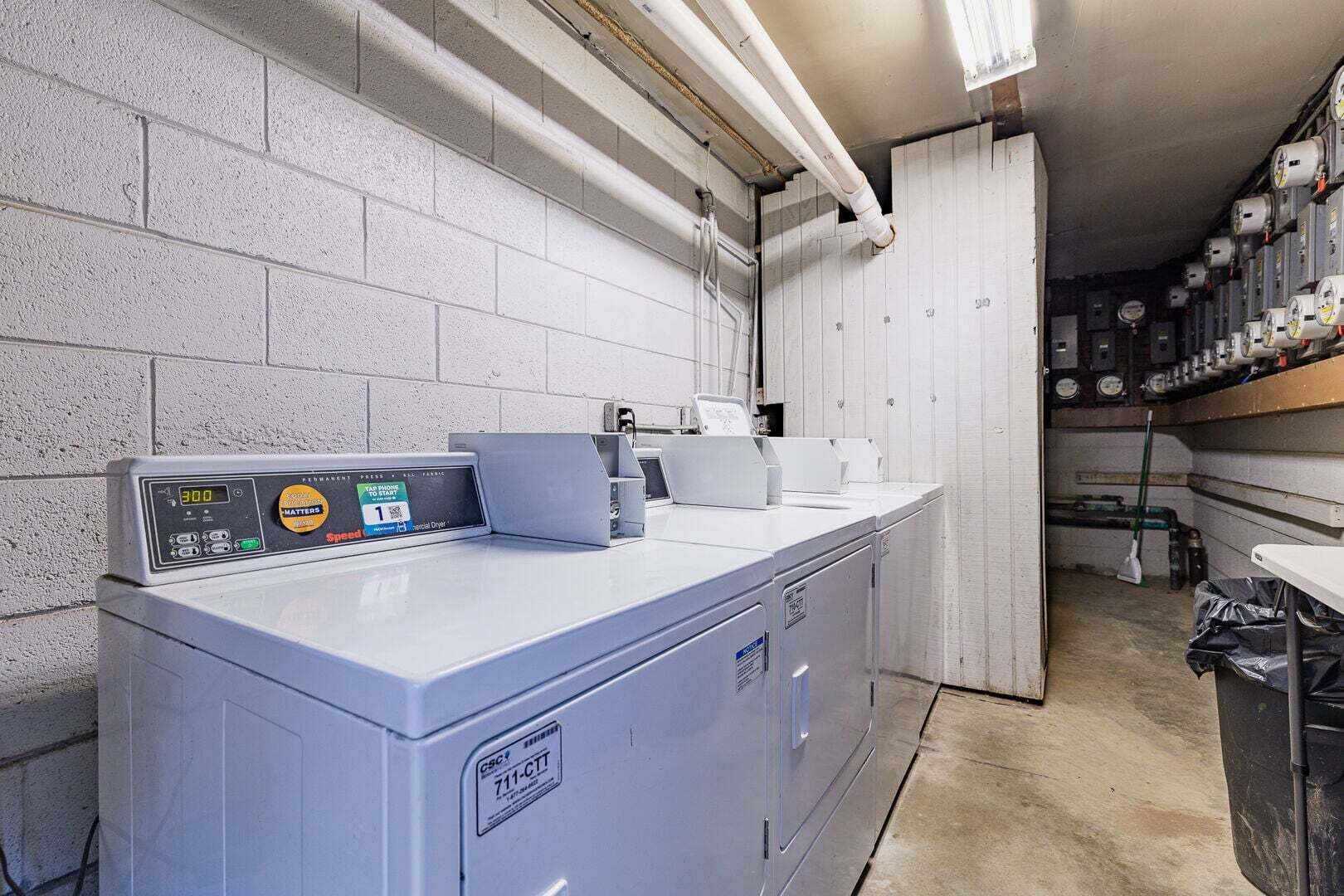 A laundry facility with industrial washing machines, a control panel, and a storage area for laundry supplies.