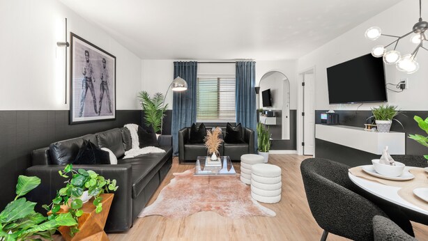 Un salon moderne avec un canapé en cuir noir, une table basse en verre et un coin repas comprenant une table et des chaises blanches.