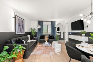 Ein modernes Wohnzimmer mit einer schwarzen Ledersofa, einem Glastisch und einem Essbereich mit weißem Tisch und Stühlen.
