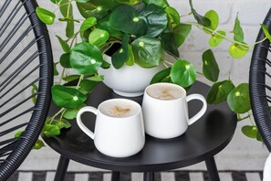 A small round table with two white ceramic cups on it, surrounded by green leafy plants.