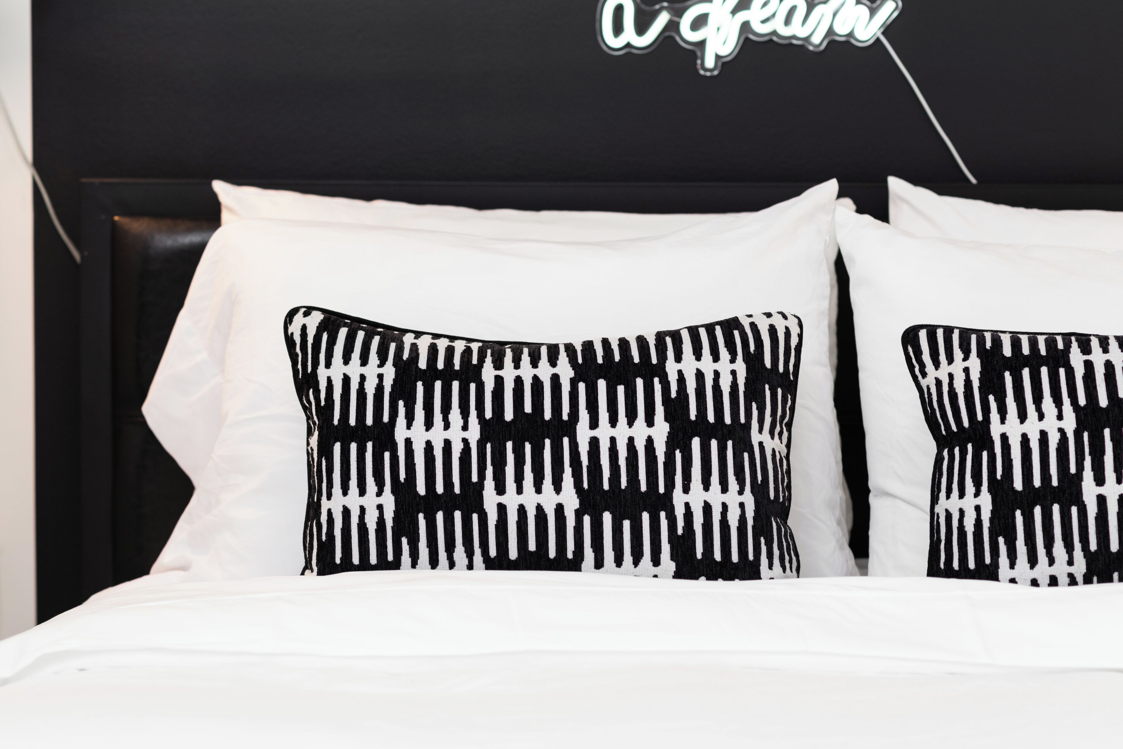 A bed with white bedding and black and white patterned pillows.