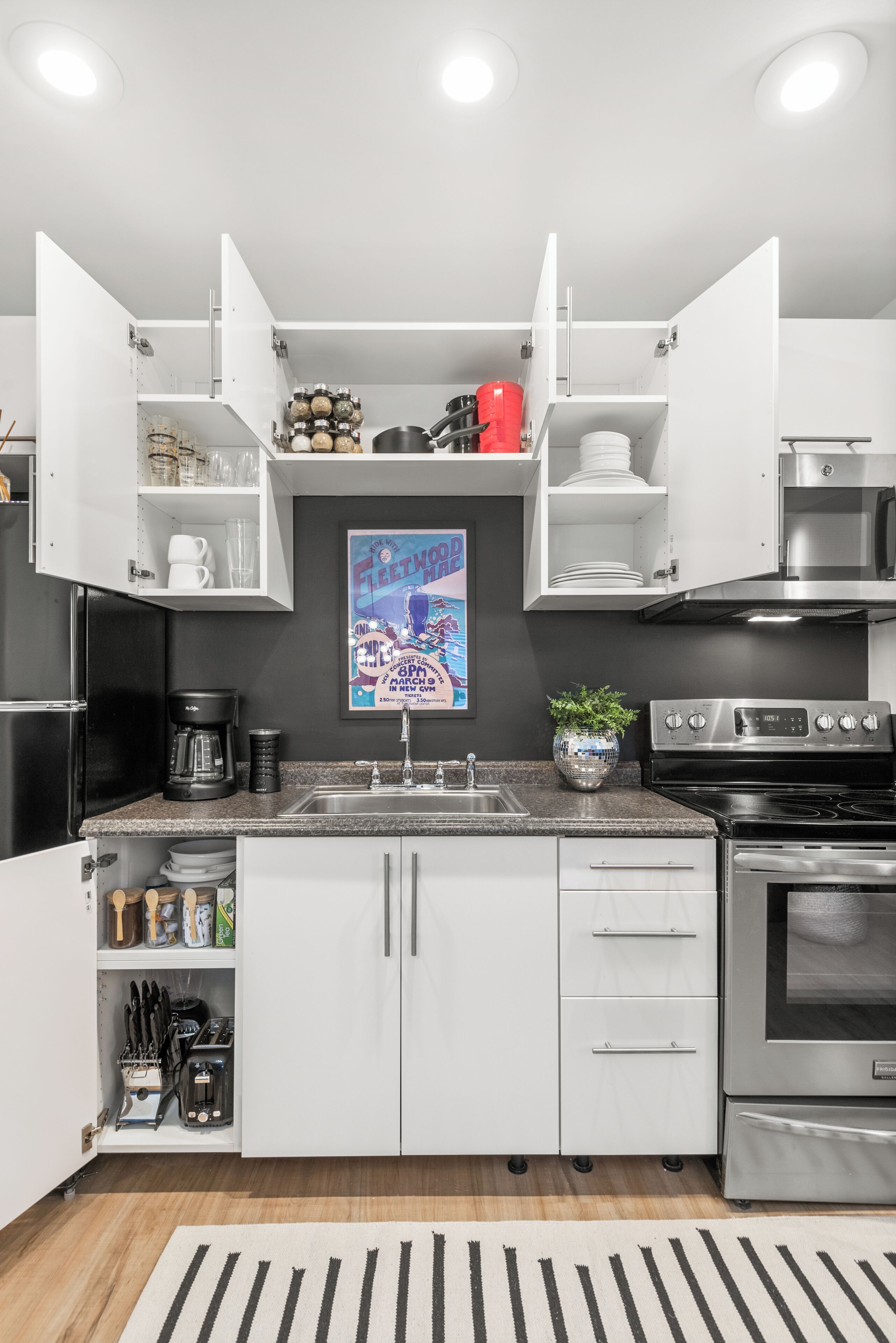 Una cocina moderna con armarios blancos, estufa de acero inoxidable y cafetera.