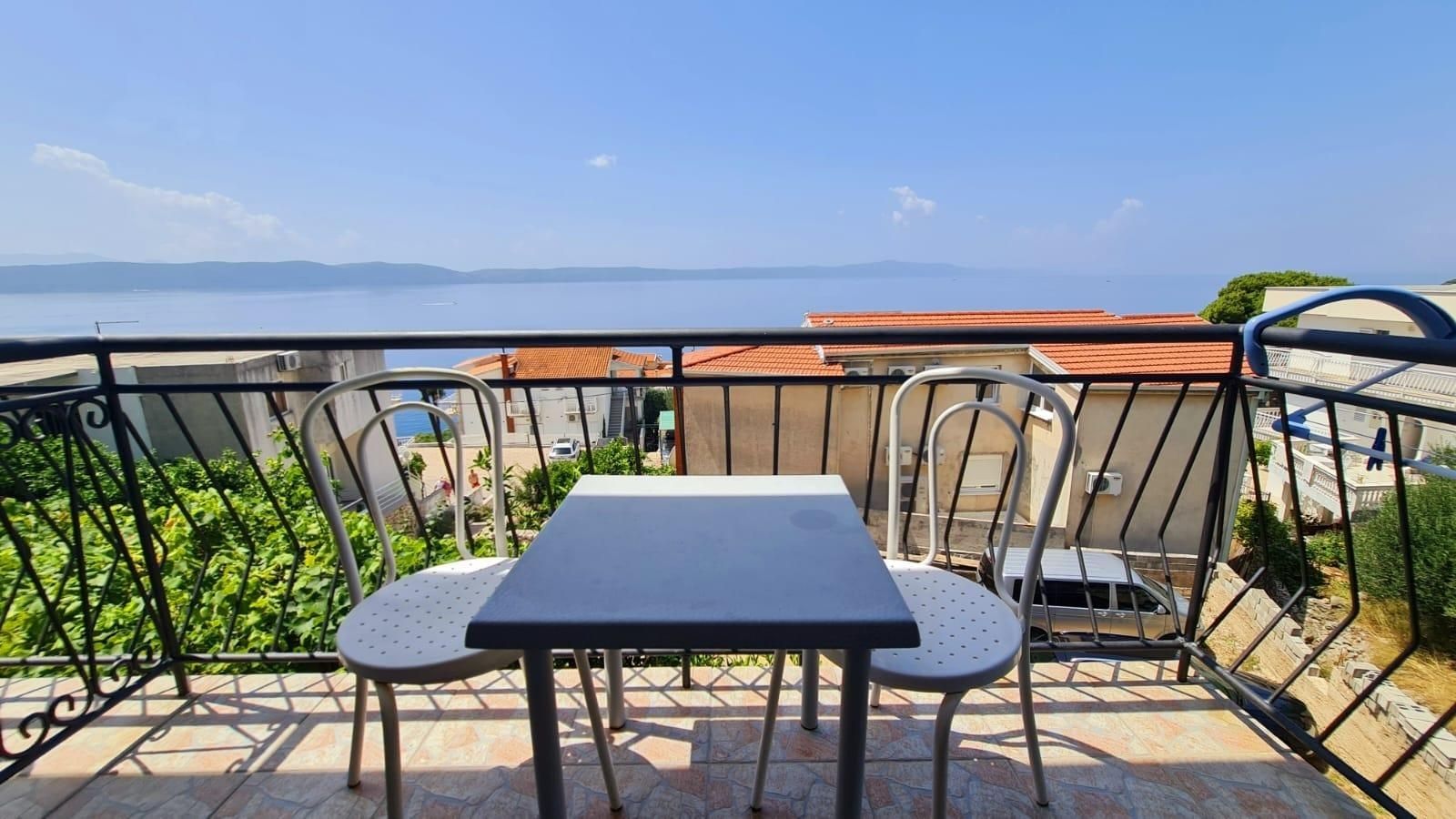 A balcony with a table and chairs, overlooking a body of water and distant hills.