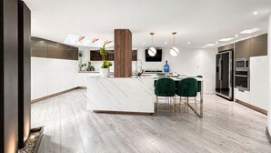 A modern kitchen with a marble island, green bar stools, stainless steel appliances, and a large wooden column.