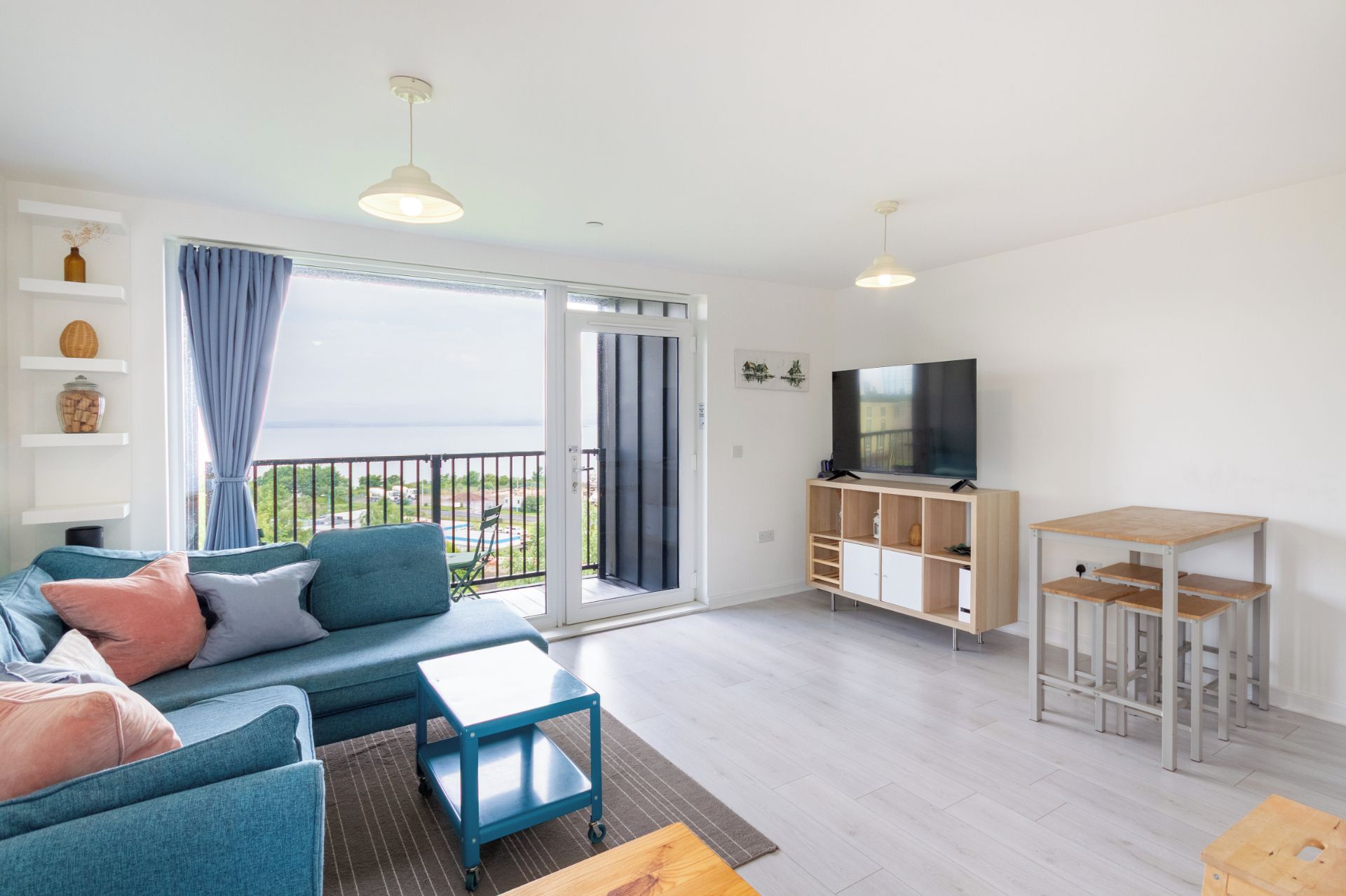A modern living room with a sofa, TV, and a balcony with a view.