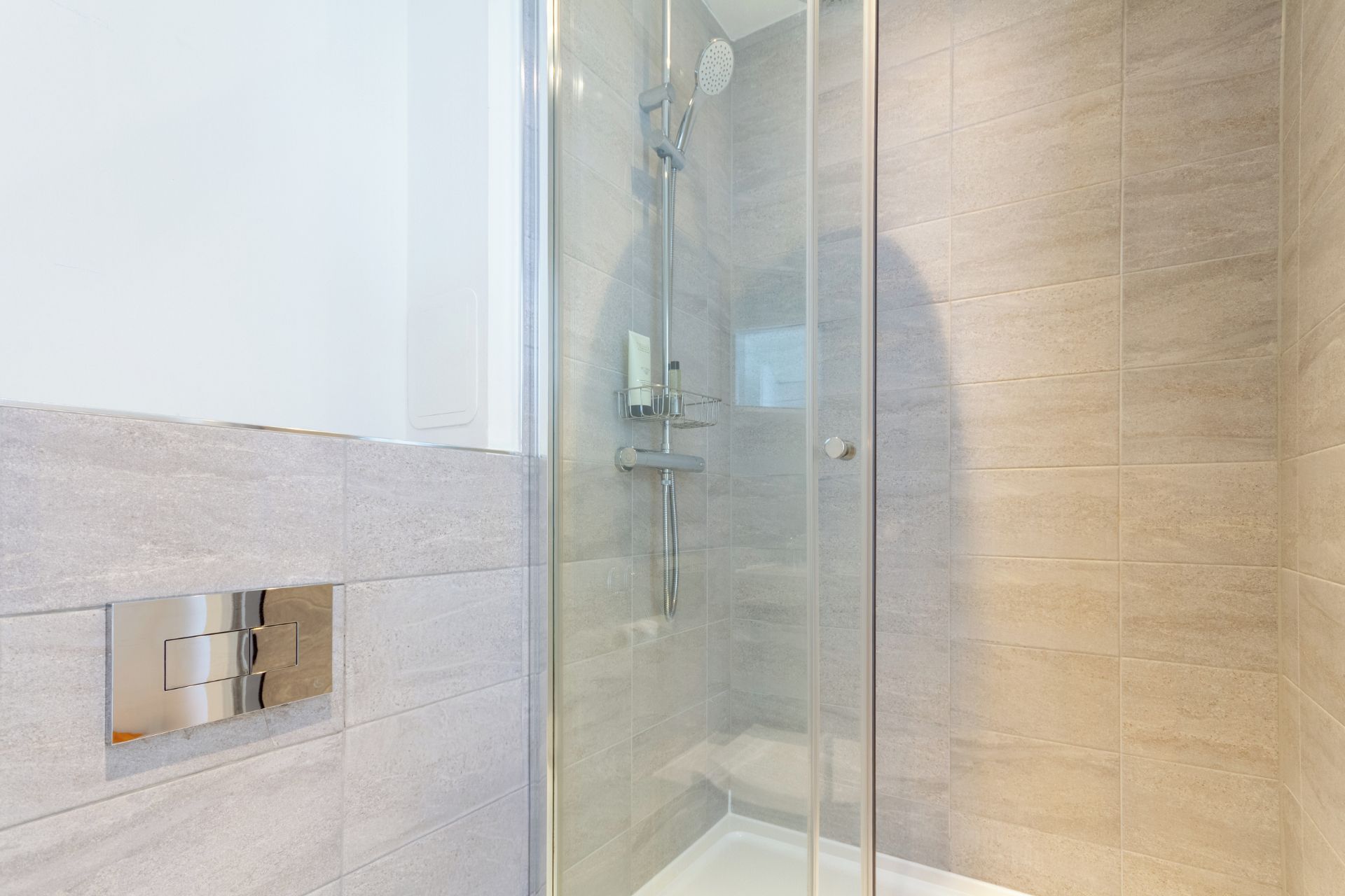 A modern bathroom with a glass shower enclosure, a white bathtub, and beige tiles.