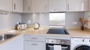 A modern kitchen with grey cabinets, a stainless steel range hood, a built-in dishwasher, and a washing machine. - Lovely Sea View 2BDR Flat in Edinburgh (Edinburgh)