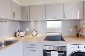 A modern kitchen with grey cabinets, a stainless steel range hood, a built-in dishwasher, and a washing machine. - Lovely Sea View 2BDR Flat in Edinburgh (Edinburgh)