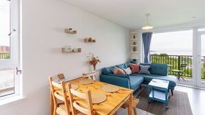 A modern living room with a wooden dining table, blue sofa, and a balcony with a view. - Lovely Sea View 2BDR Flat in Edinburgh (Edinburgh)
