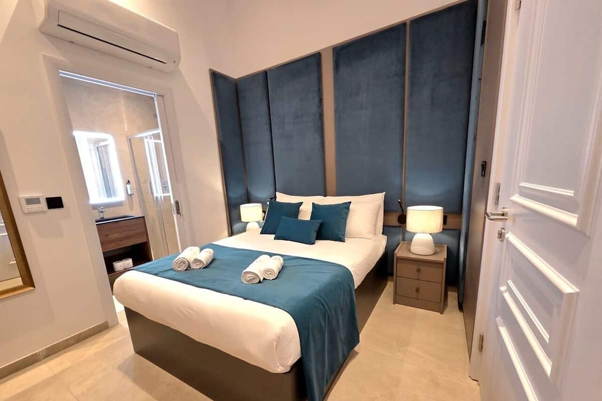 Una habitación de hotel moderna con una cama grande, mesitas de noche, un espejo y un equipo de aire acondicionado.