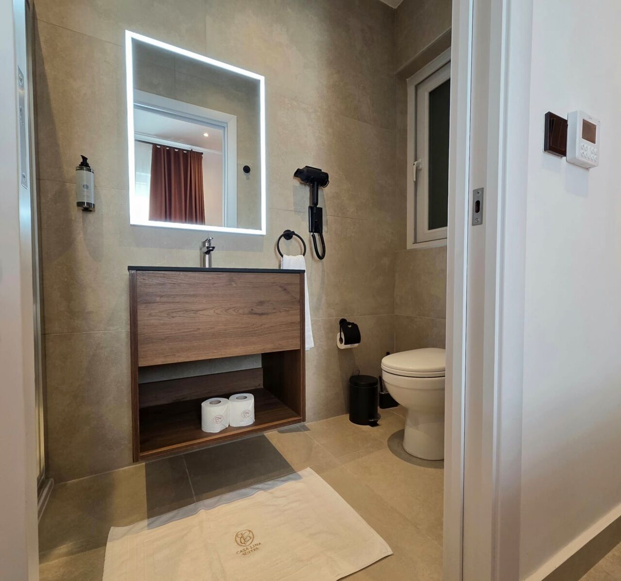 Un baño moderno con tocador de madera, espejo con luz, inodoro y secador de pelo.