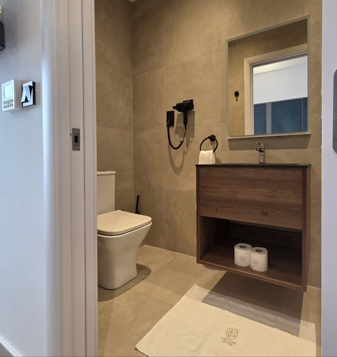 Un baño con inodoro, lavamanos con espejo y un perchero para toallas.