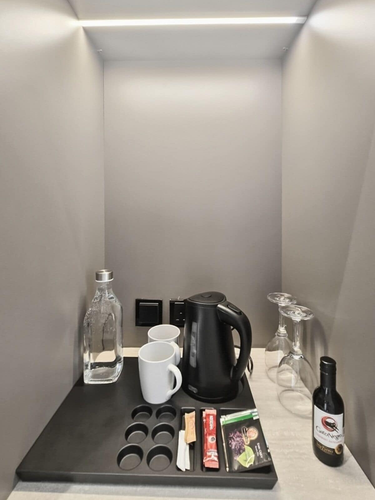 Eine kleine Küchenzeile mit Kaffeemaschine, Tassen, einer Flasche und einer Weinflasche.