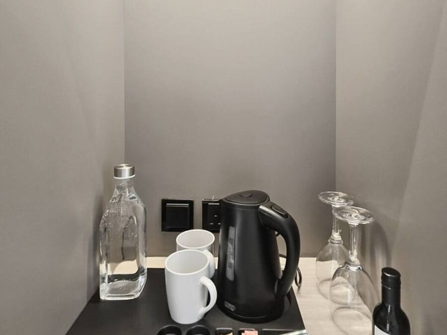 Una kitchenette compacta con cafetera, tazas, una botella y una botella de vino.
