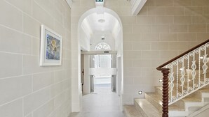 Um corredor com escada, paredes revestidas de azulejos brancos e um quadro na parede à esquerda.