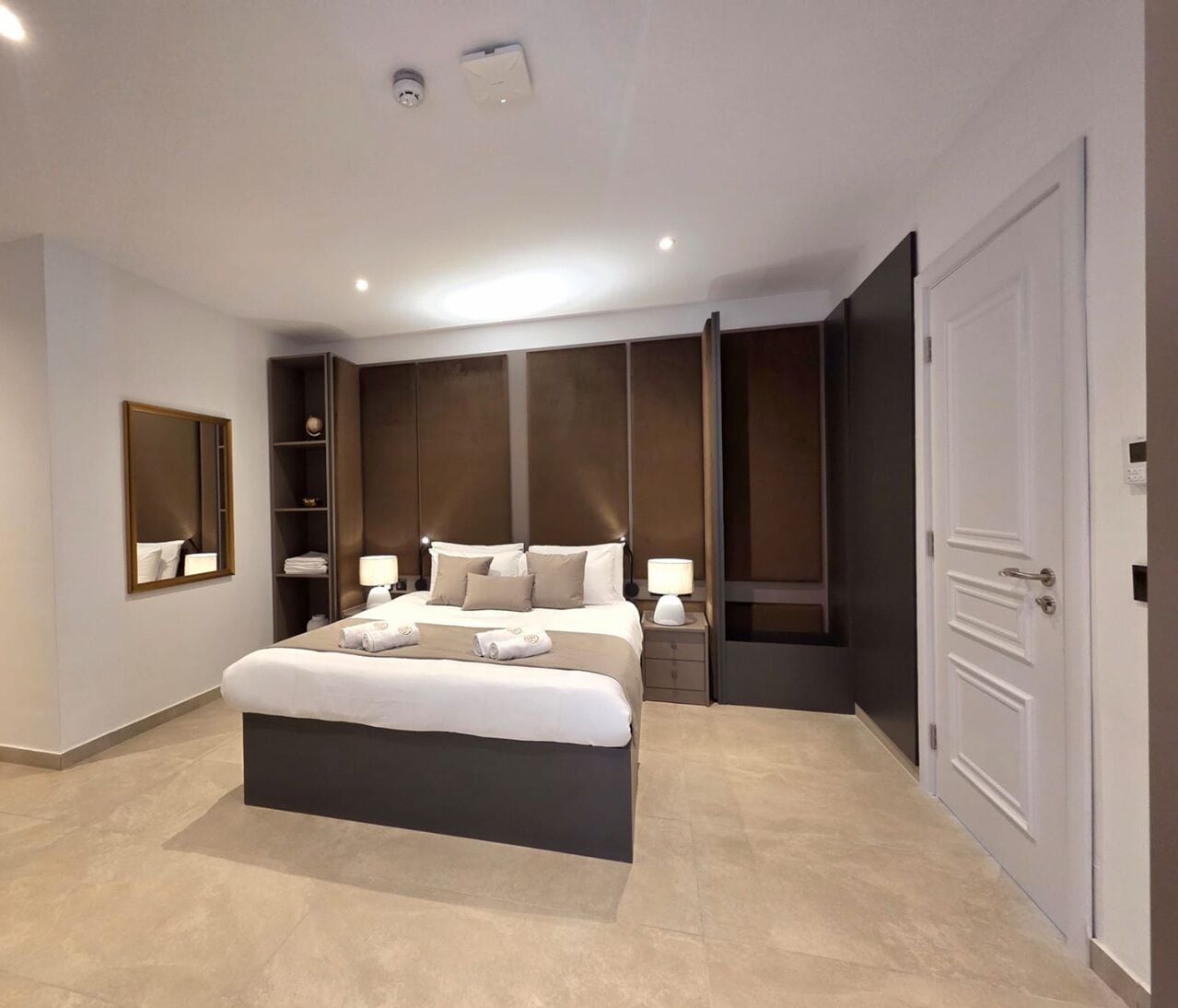 Un dormitorio moderno con una cama grande, estanterías empotradas, un armario y un espejo.