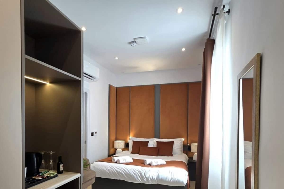 Una habitación de hotel con cama, mesitas de noche, armario y espejo.