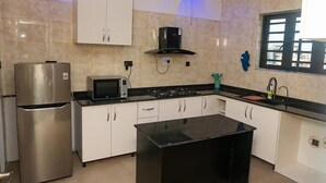A kitchen with white cabinets, a black countertop, a stainless steel refrigerator, a microwave, and a gas stove. - City-Chic Ikeja 2BR Escape: 24/7 Power, Fast WiFi, Airport, Shops & Eats - Lagos (Ikeja)