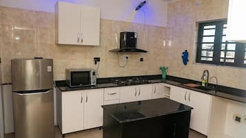 Une cuisine avec des meubles blancs, un plan de travail noir, un réfrigérateur en acier inoxydable, un four à micro-ondes et une cuisinière à gaz.
