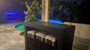 Zona de bar al aire libre con piscina, taburetes de bar y vistas nocturnas de la piscina.