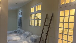 Una habitación con una cama cubierta con plástico protector, una escalera y ventanas grandes con múltiples paneles.