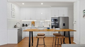 Una cocina moderna con armarios blancos, una mesa de madera, taburetes de bar y un refrigerador de acero inoxidable.