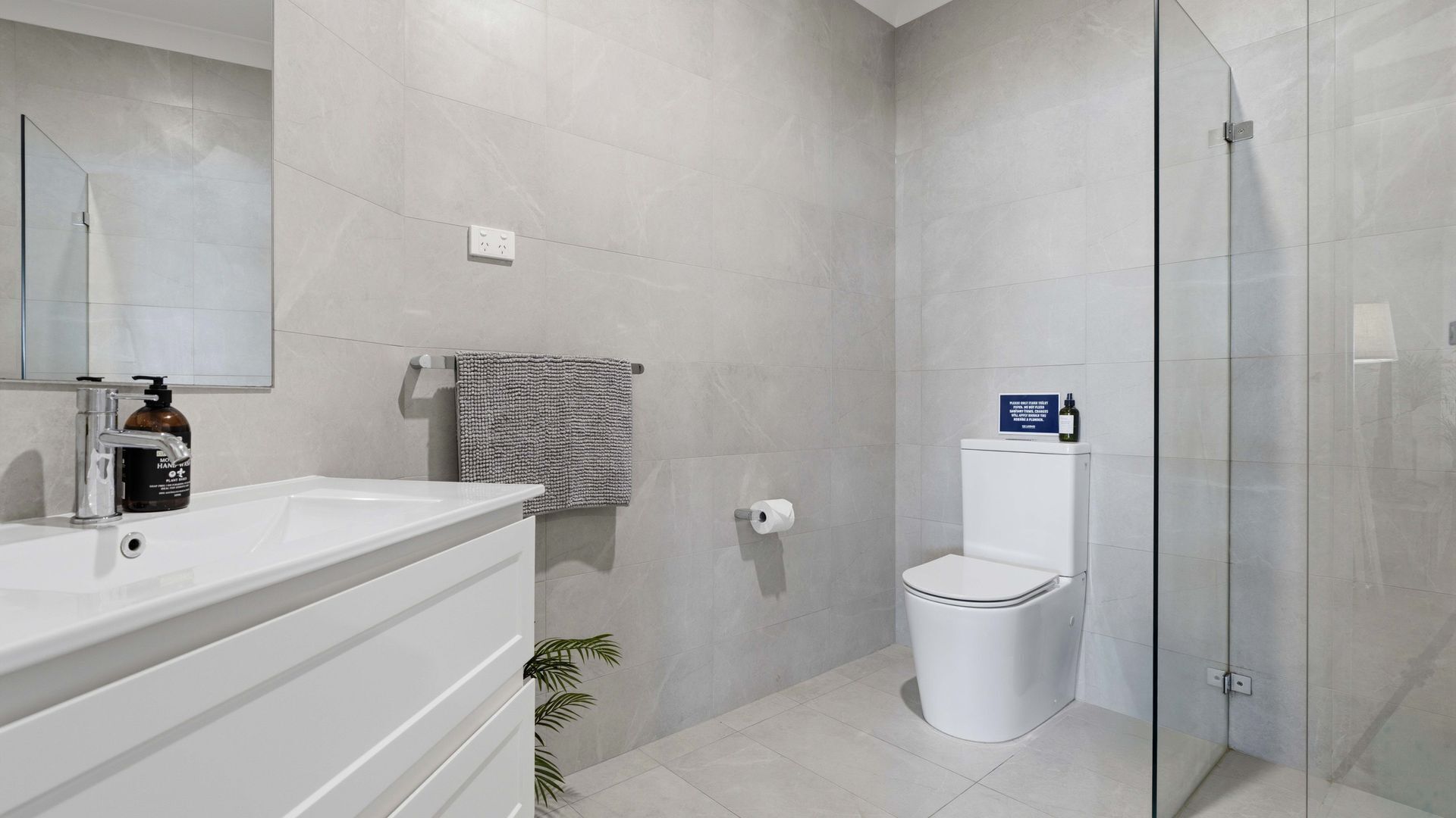 A modern bathroom with a glass shower enclosure, a white toilet, and a sink with a soap dispenser.