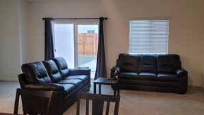 A living room with two black leather sofas, a wooden dining table, and a laptop on the table.