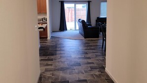 A spacious living area with a dark tiled floor, a sliding glass door leading to a backyard, and a kitchen area with wooden cabinets.
