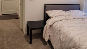 A bedroom with a bed, a nightstand, a door, and a light switch on the wall.