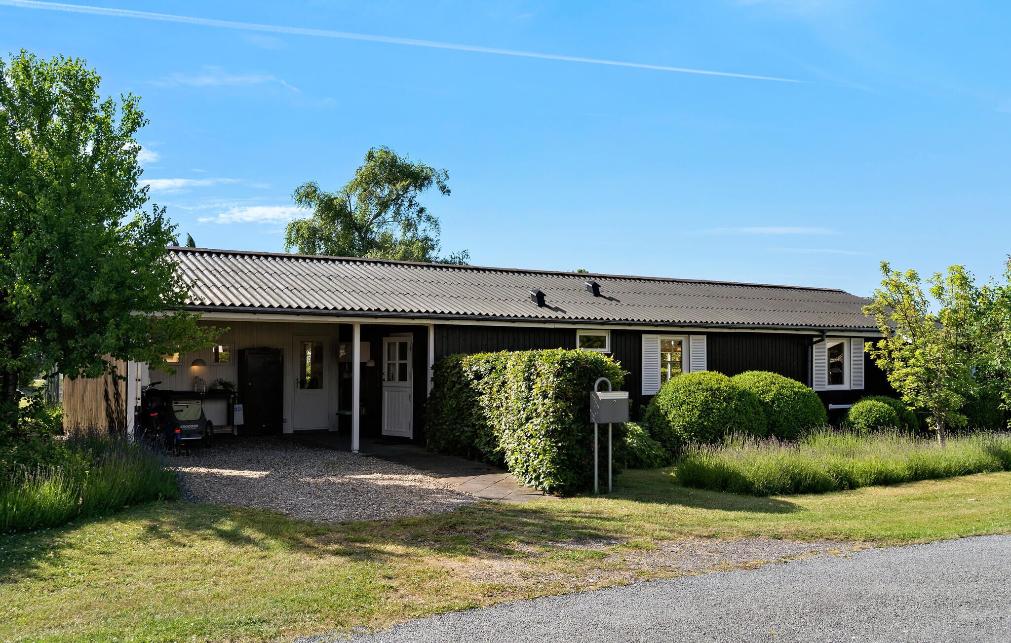 A single-story building with a porch, a gravel driveway, and a mailbox.
