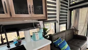 Une cuisine de taille réduite, dotée de meubles en bois, d’un plan de travail noir et d’une fenêtre avec des stores.