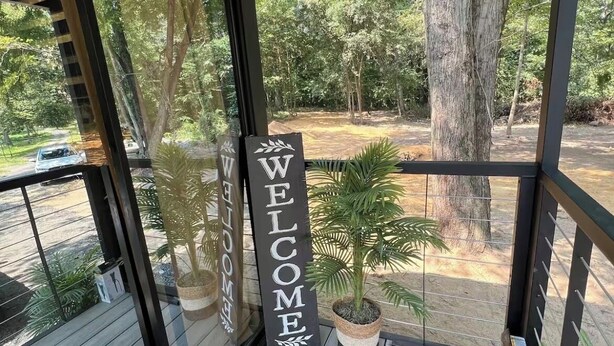 Un balcon orné d’une pancarte « BIENVENUE », d’une plante en pot et offrant une vue sur une zone bordée d’arbres.