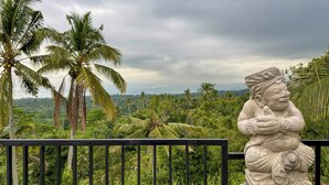 Estátua de uma figura com a mão levantada, rodeada por vegetação exuberante e palmeiras, com um céu nublado acima.
