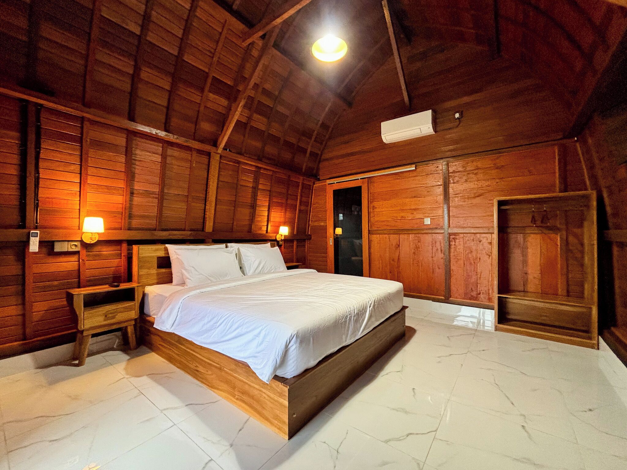 Una stanza in legno con un letto, comodini e una porta.