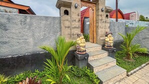 Uma entrada de pedra com degraus, duas estátuas e um edifício com telhado vermelho ao fundo.