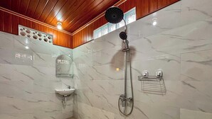 Uma casa de banho com chão de mármore, lavatório, espelho, chuveiro com chuveiro manual e um porta-toalhas.