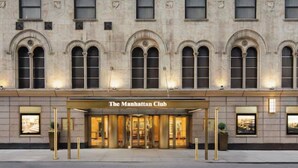 Ein Gebäude im klassischen Stil mit bogenförmigen Fenstern und einem markanten Eingang, auf dem 'The Manhattan Club' steht.
