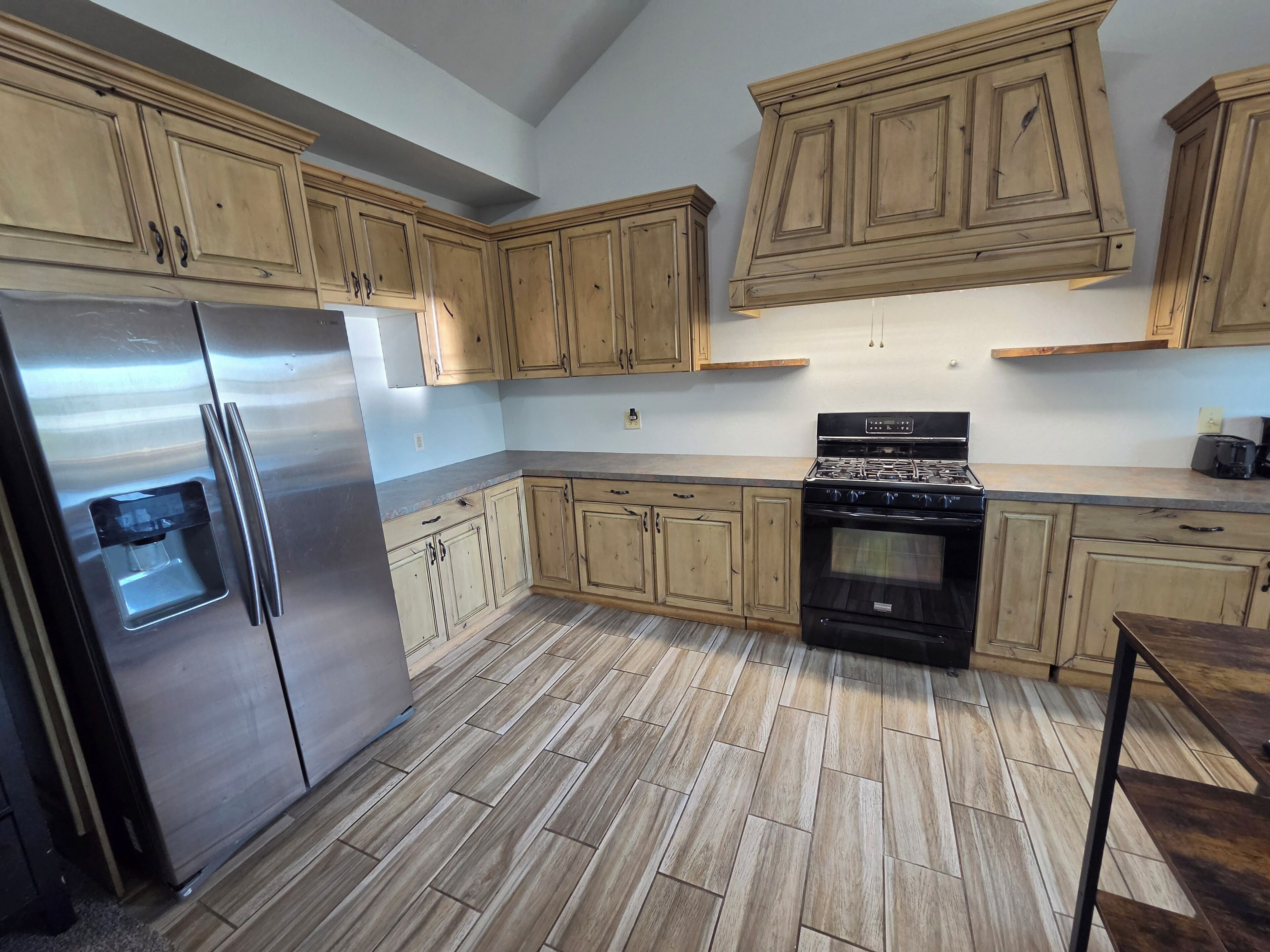 A kitchen with wooden cabinets, a stainless steel refrigerator, a stove, and a tiled floor.