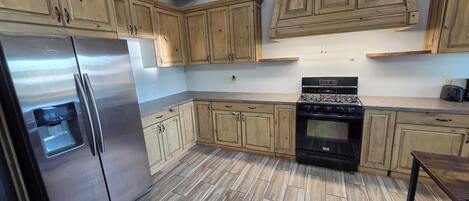 A kitchen with wooden cabinets, a stainless steel refrigerator, a stove, and a tiled floor.