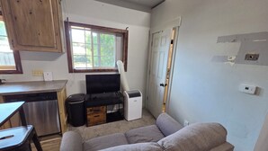 A compact living space with a kitchenette, a sofa, a small dining table, and a window.