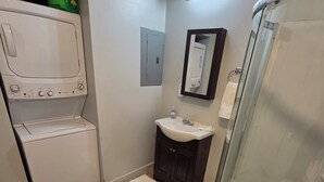A bathroom with a washing machine, a sink, a mirror, and a shower.